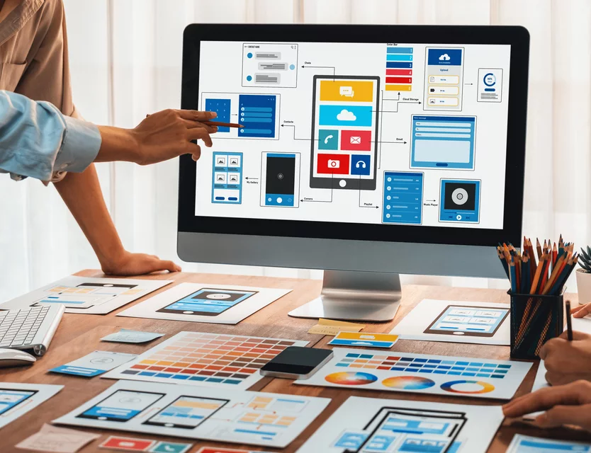 A design team reviewing app wireframes and screen layouts on a monitor and on paper